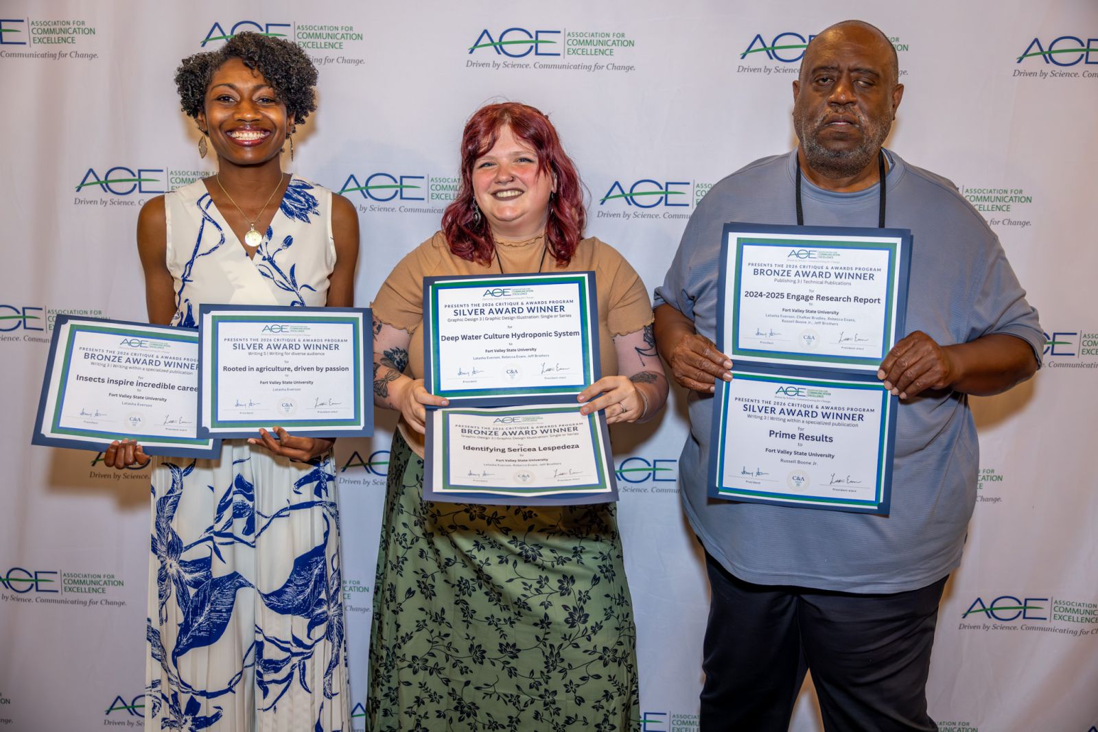 Three people holding six awards in front of backdrop