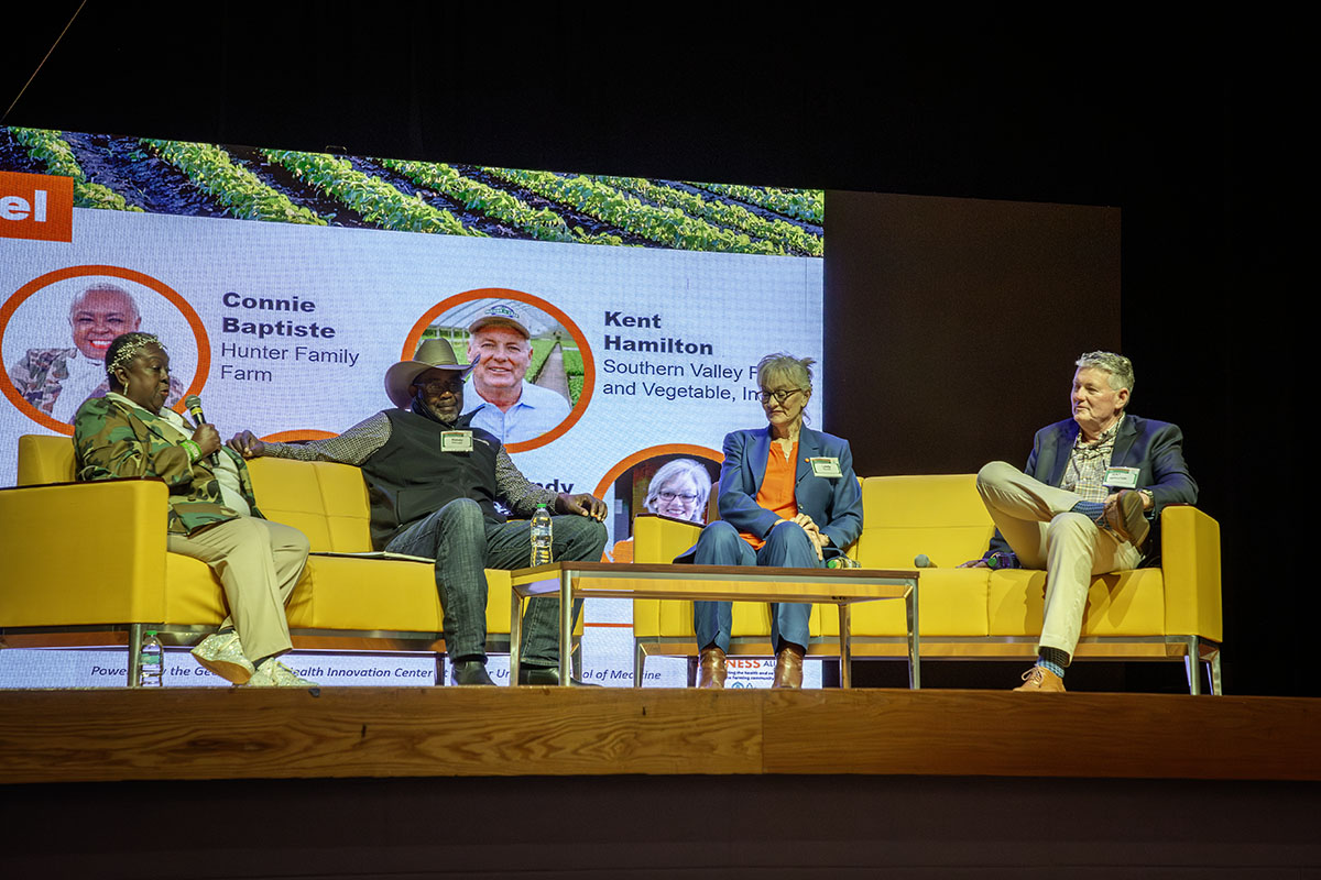 four people seated on yellow couches on stage with a video backdrop.