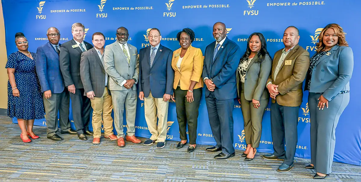 FVSU admininstrators as well as elected officials smile for a grop photo in front of an FVSU themed backdrop.