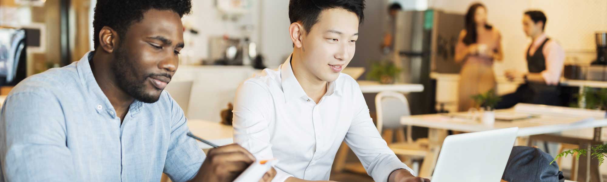 Two college students seated at classroom table looking at laptop